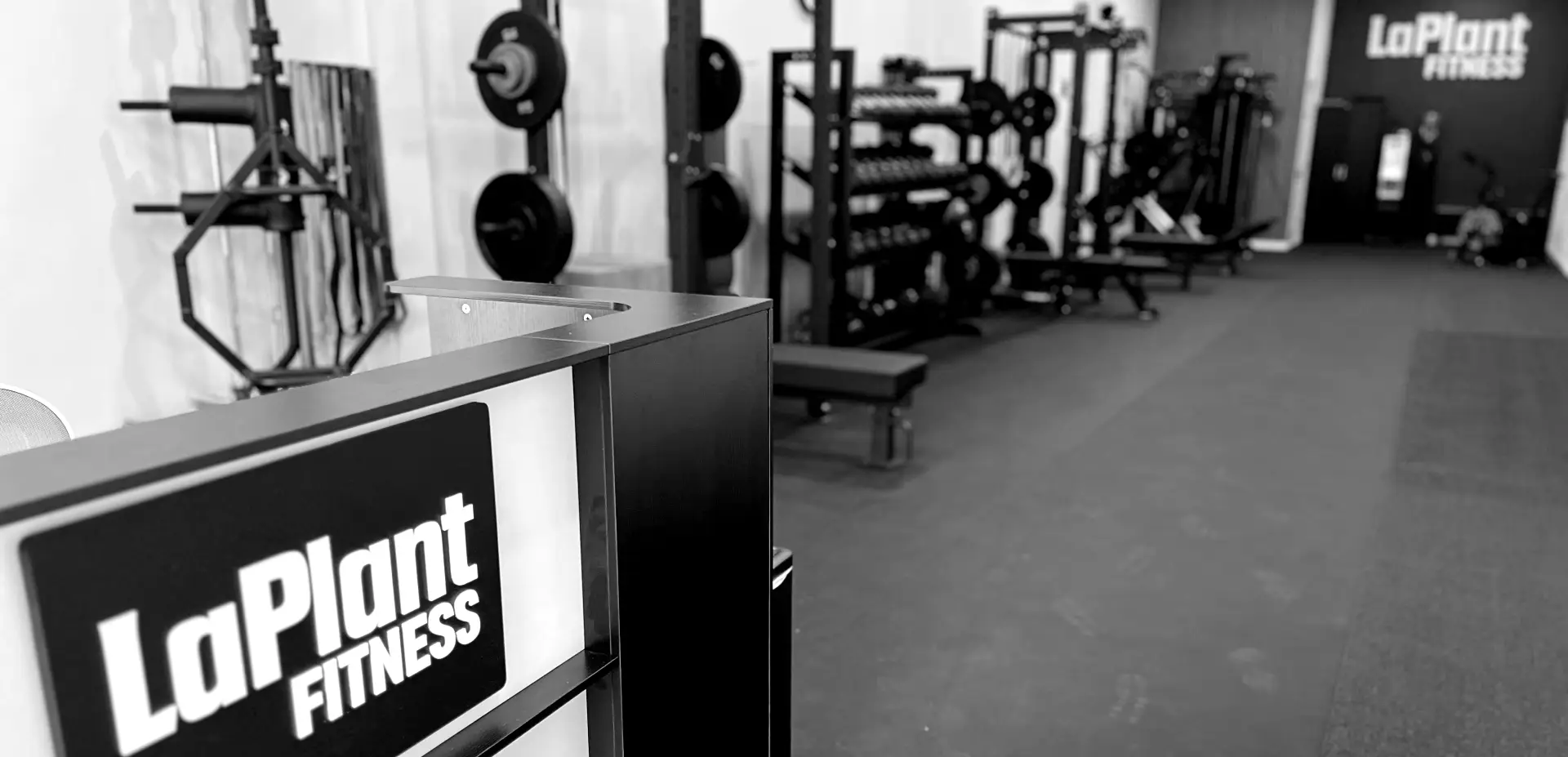 Interior panoramic view of LaPlant Fitness personal training gym in Marin, showing the weightlifting area with squat racks, benches, and the branded reception desk